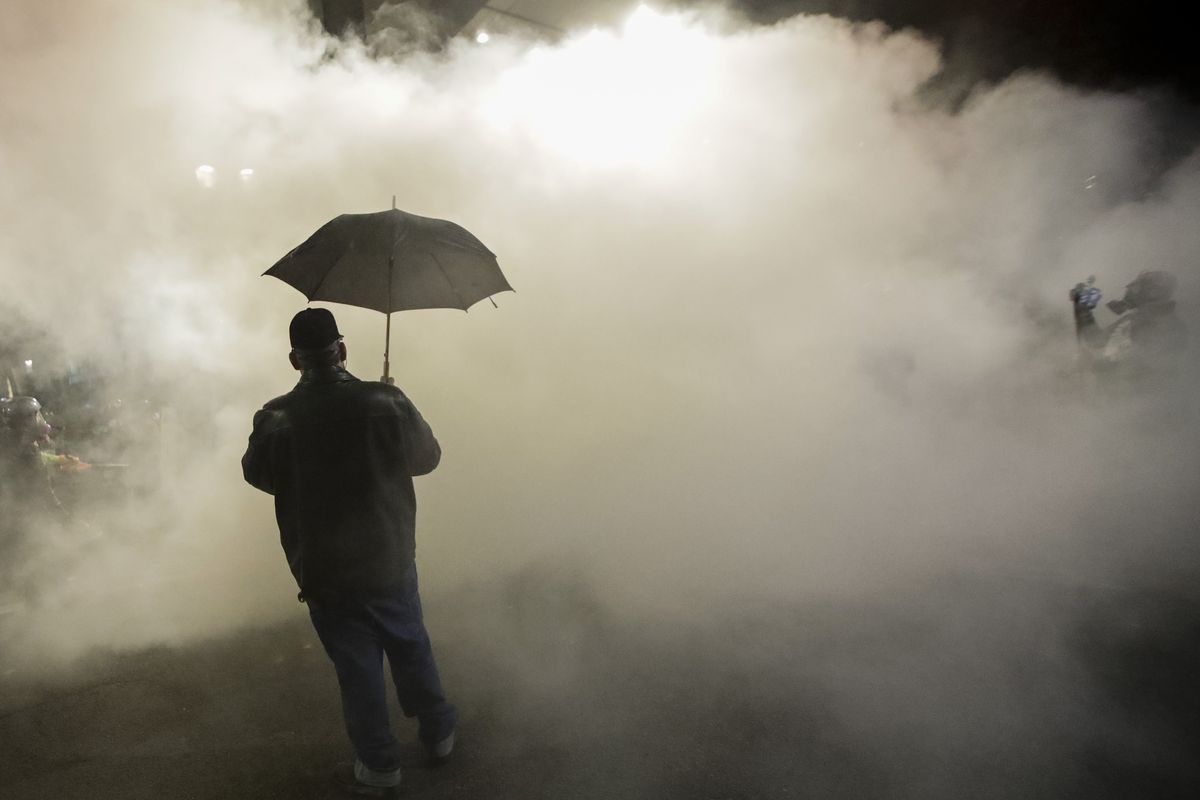 In this July 25, 2020, file photo, a protester carries an umbrella as federal police officers deploy tear gas during a protest at the Mark O. Hatfield U.S. Courthouse in Portland, Ore. Federal agents have left Portland, but city officials are still learning about and cleaning tear gas residue that lingers in the streets, dirt and possibly storm drains that empty into the Willamette River. (Associated Press)