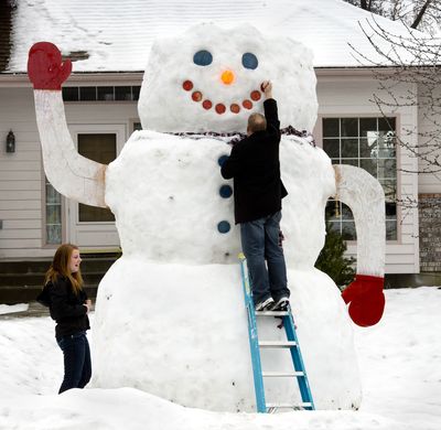 Restoration work: JC Conrad, 44, of Spokane Valley, pounds a painted plywood piece back into the smile of his giant snowman Friday. The warming temperatures caused the wood to drop. Conrad, along with his daughter, Asia, 19, left, and other family members used 5-gallon buckets to collect snow from neighbors’ driveways in the 13900 block of East 26th Avenue to add to the snowman’s height and bulk. (Dan Pelle)