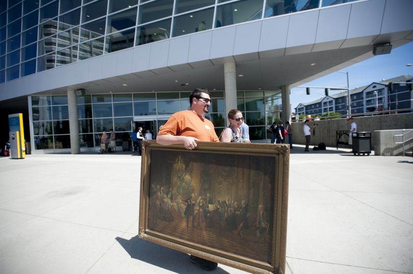 Mike Lish and his wife, Erin, carry a painting they had appraised at “Antiques Roadshow” Saturday in Spokane. “A Flute Concert of Frederick the Great at Sanssouci,” which the family thought was an original by Adolph von Menzel, turned out to be a copy. (Tyler Tjomsland)