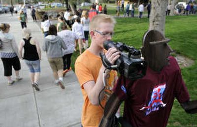 
Chris Klok, 18, of Edmonton Christian School, uses a Bloomsday statue to steady his camera while filming members of his group downtown on Friday. 
 (Photos by DAN PELLE / The Spokesman-Review)