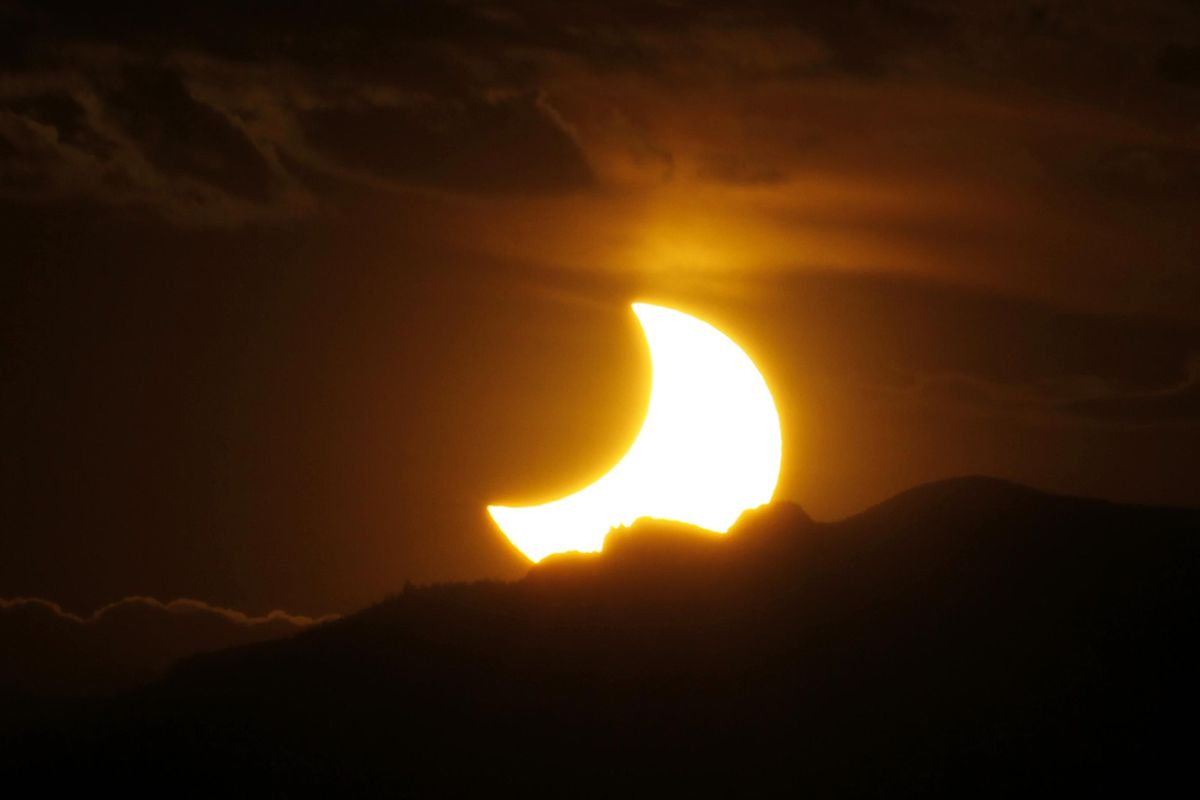 In this May 20, 2012, file photo, the annular solar eclipse is seen as the sun sets behind the Rocky Mountains from downtown Denver. Destinations are hosting festivals, hotels are selling out and travelers are planning trips for the total solar eclipse that will be visible coast to coast on Aug. 21, 2017, but the Department of Transportation is warning of the possibility of extreme congestion on the highways as people transit Washington on their way south to Oregon. (David Zalubowski / AP)