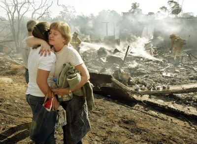 Barbara Pointer and her daughter Katie embrace Friday morning as firefighters extinguish the last flames from their Montecito, Calif., home, background, destroyed in a wildfire that began Thursday.  (Associated Press / The Spokesman-Review)