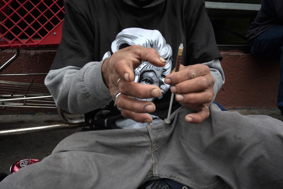 A drug addict prepares a needle to inject himself with heroin in front of a church in the Skid Row area of Los Angeles last May. (Associated Press)