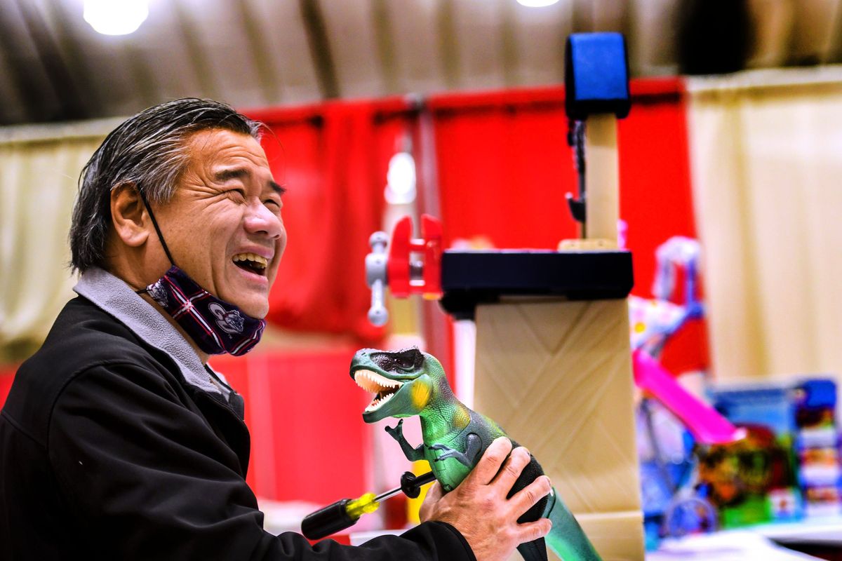 Volunteer Damon Taam shares a laugh as he adds batteries to a toy dinosaur for the Christmas Bureau on Tuesday at the Spokane Fair and Expo Center.  (Kathy Plonka/The Spokesman-Review)