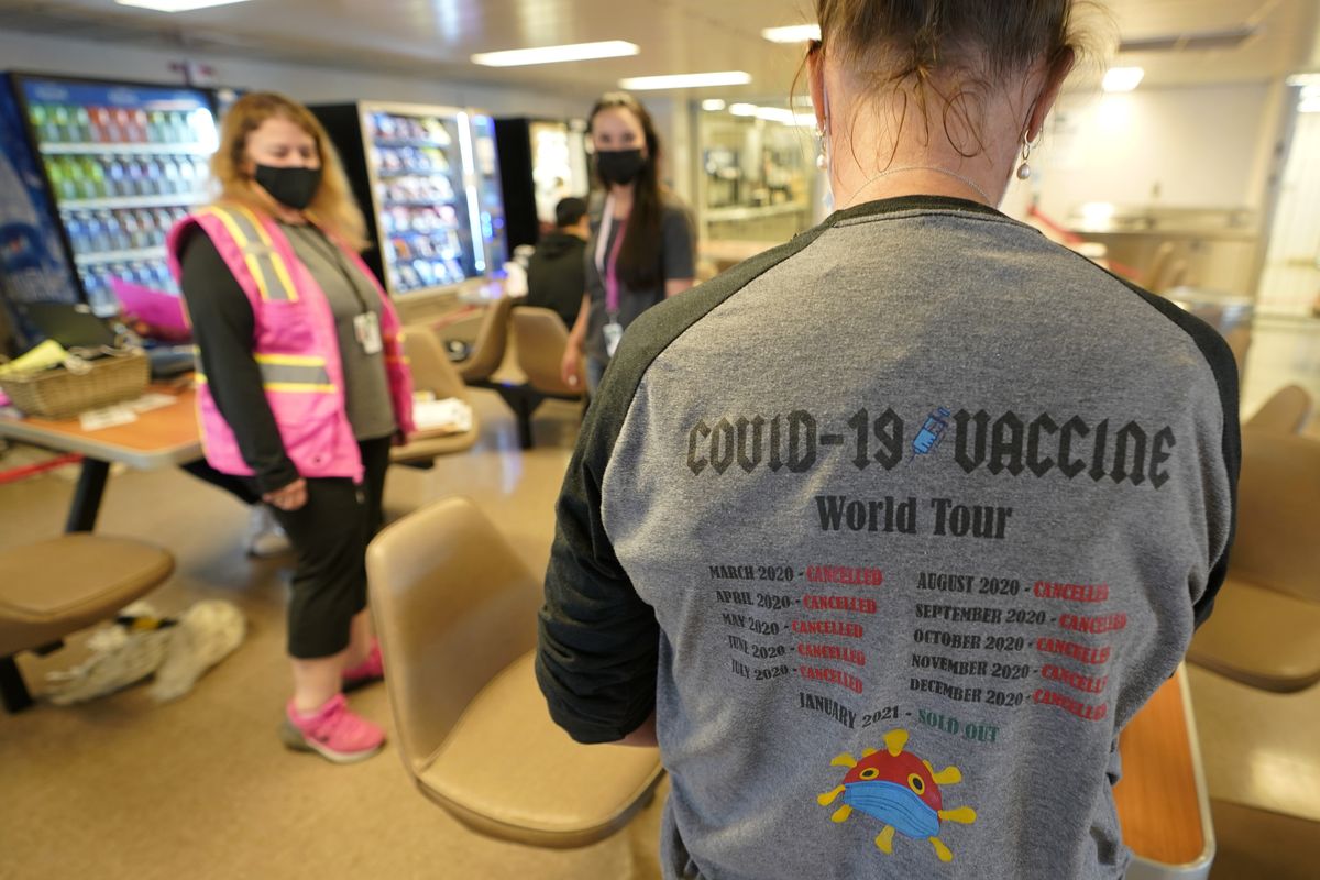 Amber Coole, right, a medical assistant with Peninsula Community Health Services, wears a T-shirt that reads “COVID-19 Vaccine World Tour” as she works in a clinic set up in the galley area of a Washington state ferry sailing from Bremerton, Wash. to Seattle, Tuesday, May 25, 2021. Tuesday was the first day of several dates that the vaccine will be offered to people on ferry sailings between the two cities.  (Ted S. Warren)