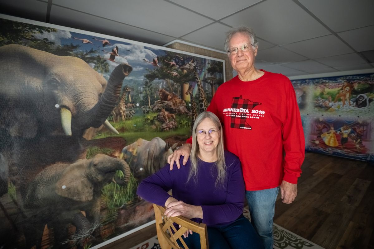 Avid puzzler and puzzle collector Linda Groskreutz, 67, poses for a portrait with her husband Jeff, 69, in front of two giant puzzles on display in her home in Madison Lake, Minnesota.  (Caroline Yang/For The Washington Post)