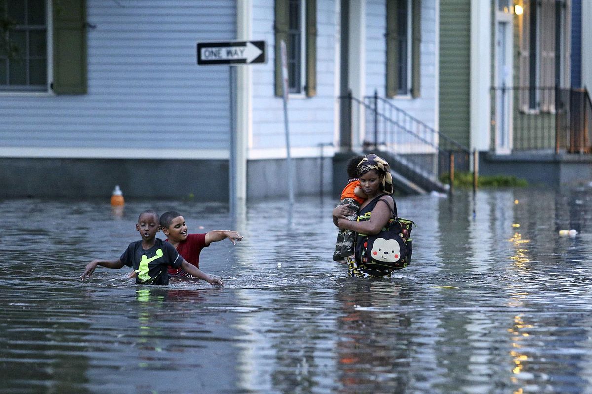 This Saturday, Aug. 5, 2017 photo shows a woman carrying an infant through floodwaters as two boys tag along in Metairie, La. (Michael DeMocker / Times-Picayune)