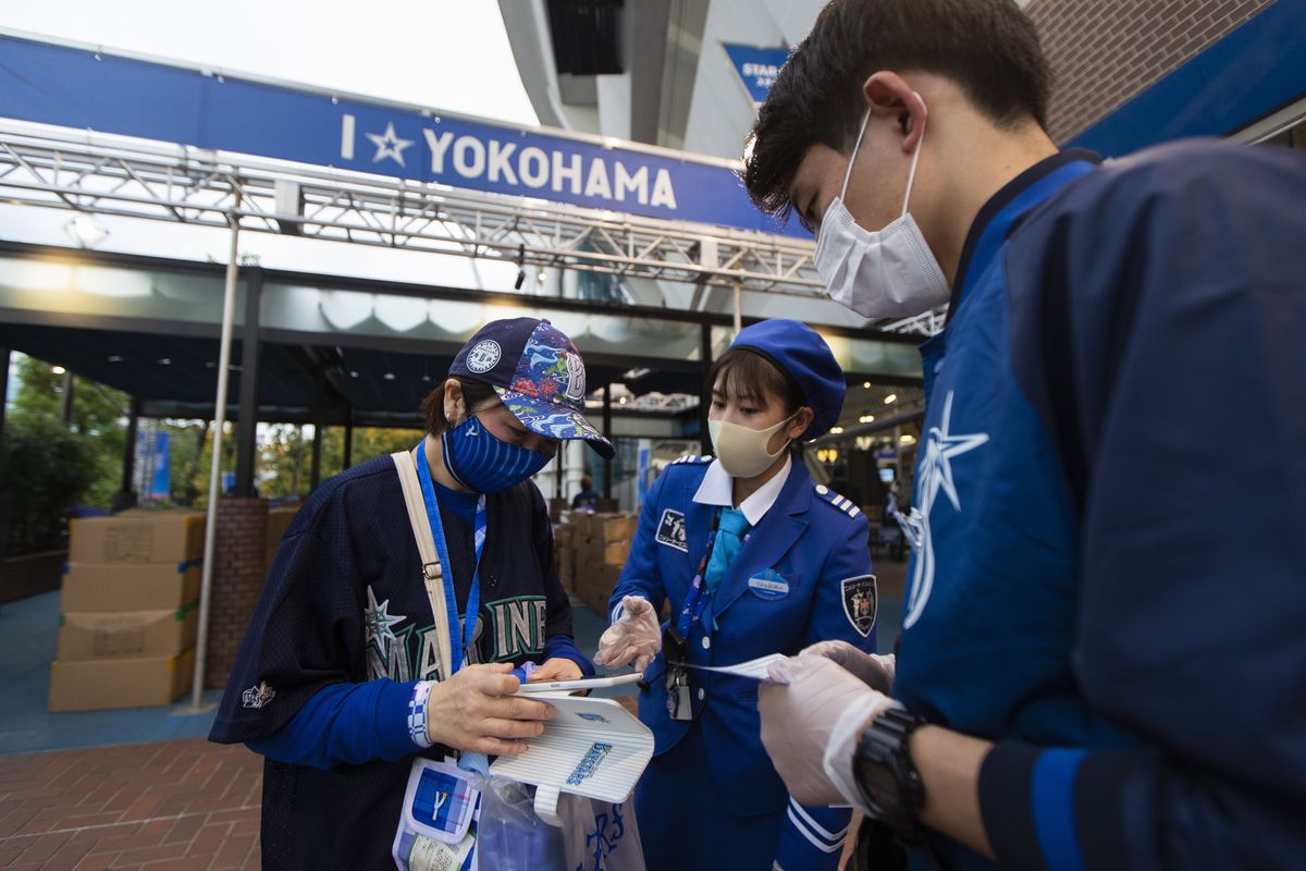 A fan tries to show a mobile phone app called Cocoa created by the Japanese health ministry to help curb the coronavirus as she enters a baseball stadium before a Japanese professional baseball league game in Yokohama, south of Tokyo on Friday, Oct. 30, 2020.  (Hiro Komae/Associated Press)
