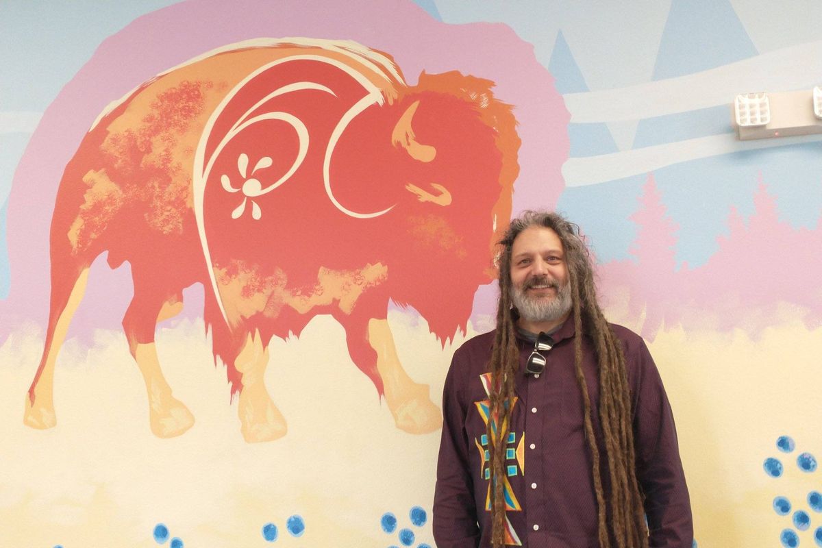Randall Schleufer stands in front of his recent art project, a mural he painted for the Gonzaga Family Haven, titled “The Language Wall.”  (Matthew Kincanon/FāVS News)
