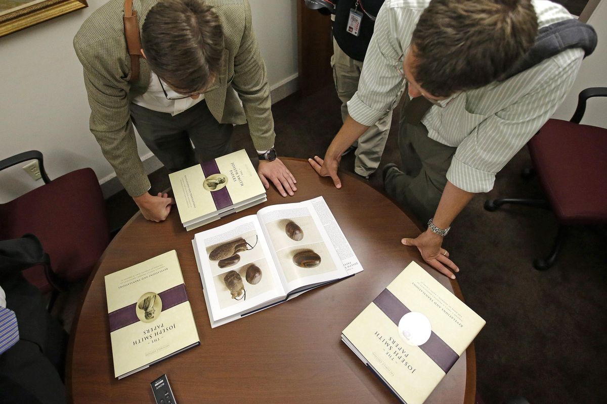 People look at pictures of the smooth, brown, egg-sized rock shown in the printer’s manuscript of the Book of Mormon following a news conference Tuesday, Aug. 4, 2015, at the Church of Jesus Christ of Latter-day Saints Church History Library, in Salt Lake City. The Mormon church for the first time is publishing photos of a small sacred stone it believes founder Joseph Smith used to help translate the story that became the basis of the religion. The Mormon church is taking another step in its push to be more transparent, and is releasing more historical documents that shed light on how Joseph Smith formed the religion. (Rick Bowmer / AP)