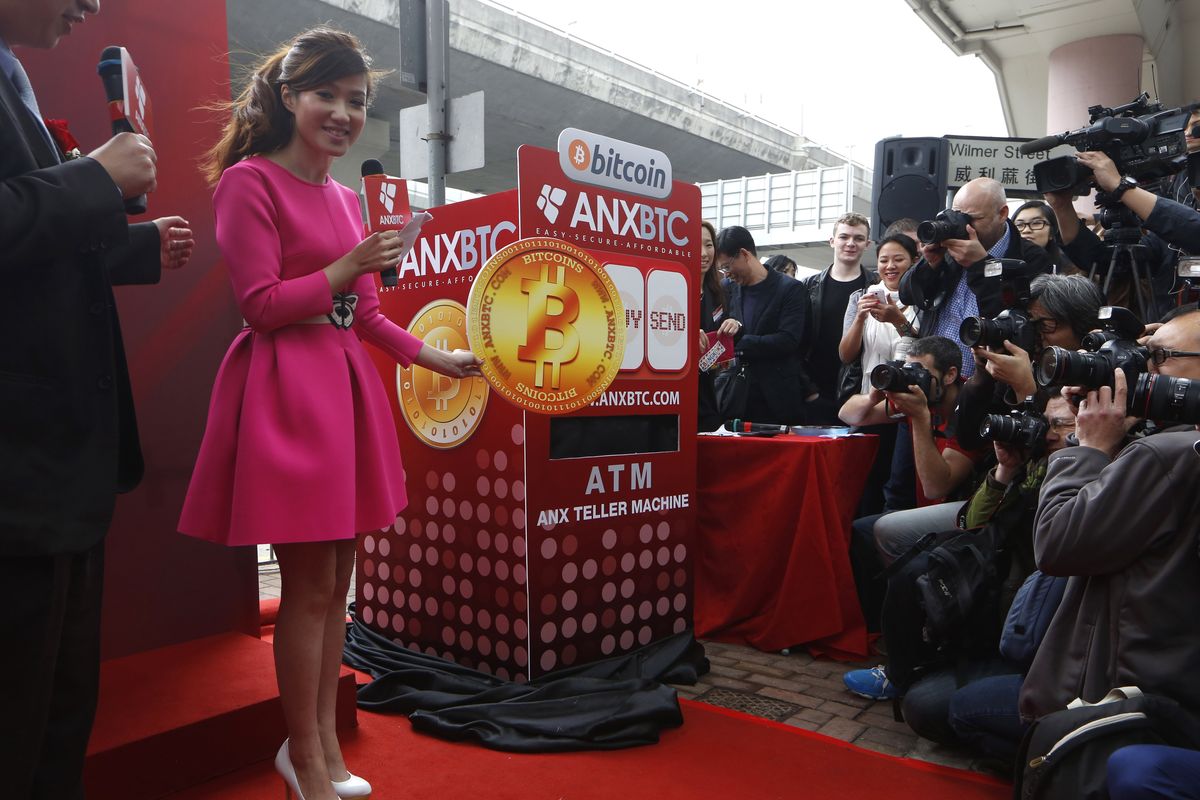 A model poses with a cardboard replica of a “bitcoin” near its ATM during the opening ceremony of an ANXBTC bitcoin retail store in Hong Kong on Friday. The world’s first bitcoin retail store opened despite the virtual currency facing much scrutiny over the past week. (Associated Press)