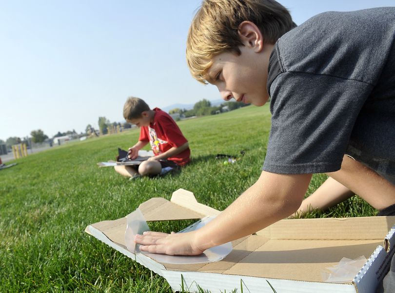 Fourth-grader Tyler Burghard, 10, right, tapes plastic into the lid of a pizza box to build a solar oven Wednesday at East Farms Elementary in Otis Orchards. The STEAM Magnet program gives students a chance to participate in a variety of projects and subjects, and the school is becoming a magnet school with the STEAM program as a theme. In the background is fellow student Hayden Ohl. (Jesse Tinsley)