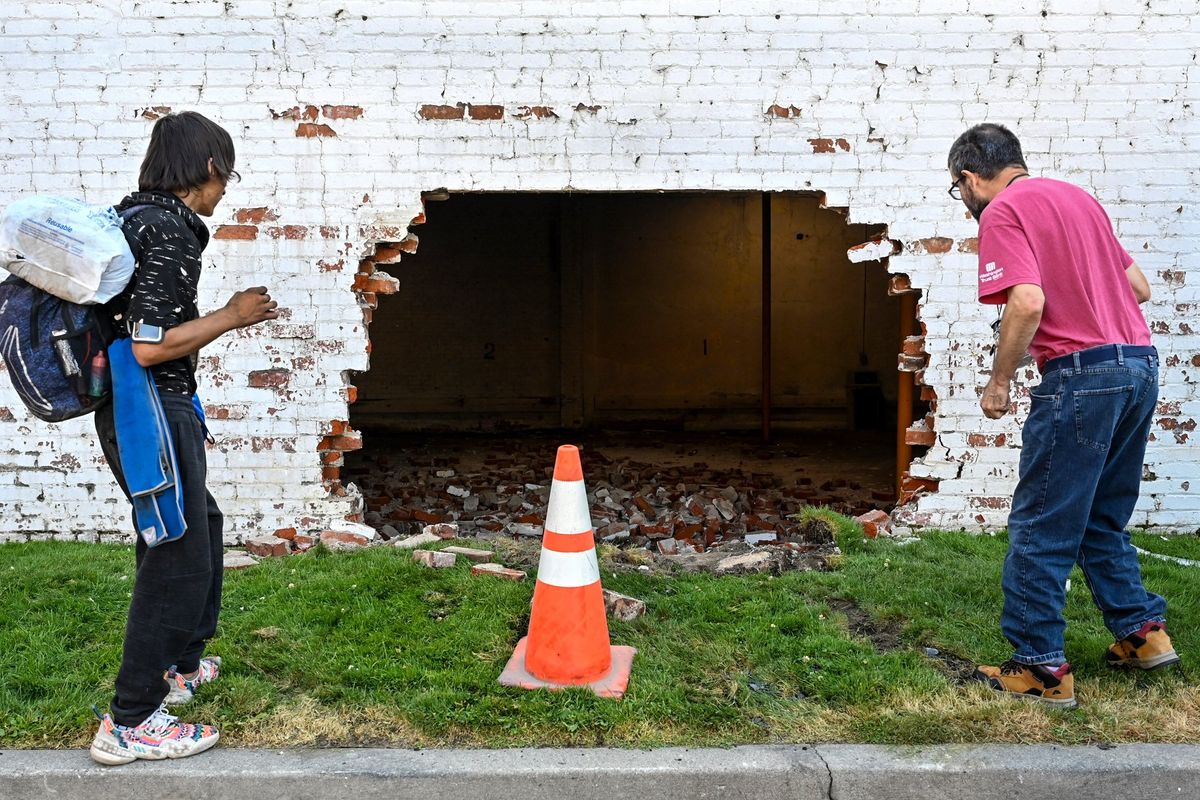 Joshua Fury, left, and Jim Friedrich get a close view after a vehicle crashed into a wall three bricks deep at the corner of Second Avenue and Lincoln Street on Thursday morning. The police chase started in Airway Heights. The driver was arrested at the scene, and multiple police cars were reported damaged.  (DAN PELLE/THE SPOKESMAN-REVIEW)