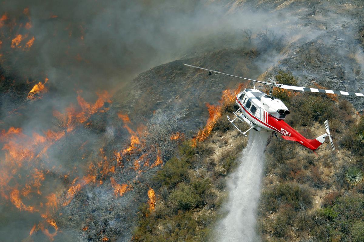 A Los Angeles County Firefighter helicopter drops water on a wildfire burning through 3,600 acres of the Angeles National Forest on Tuesday Sept. 4, 2012 near Glendora, Calif. It could be a week before firefighters can contain the blaze because of high temperatures and rugged terrain in thick brush that hasn