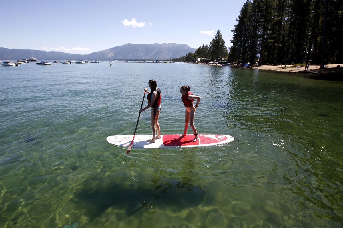 FILE - In this Aug. 20, 2019, file photo, Freya Mayo, left, and her sister Evie, of London, try out a paddle board on Lake Tahoe near South Lake Tahoe, Calif. With wildfire no longer threatening Lake Tahoe, residents, tourists and scientists drawn to its clean alpine air, clear blue waters and fragrant pine trees now wonder about the long-term effects that will remain after wildfire season ends.  (Rich Pedroncelli)