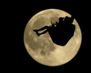 People are silhouetted against a rising full moon as they ride an attraction at Worlds of Fun amusement park Thursday in Kansas City, Mo. When the full moon appears at 6:43 a.m. EDT (1043 GMT) in the U.S. Friday, it will become the second full moon of July. Geoff Chester of the U.S. Naval Observatory said the traditional definition of a blue moon is two full moons in a month.  (Charlie Riedel / Associated Press)