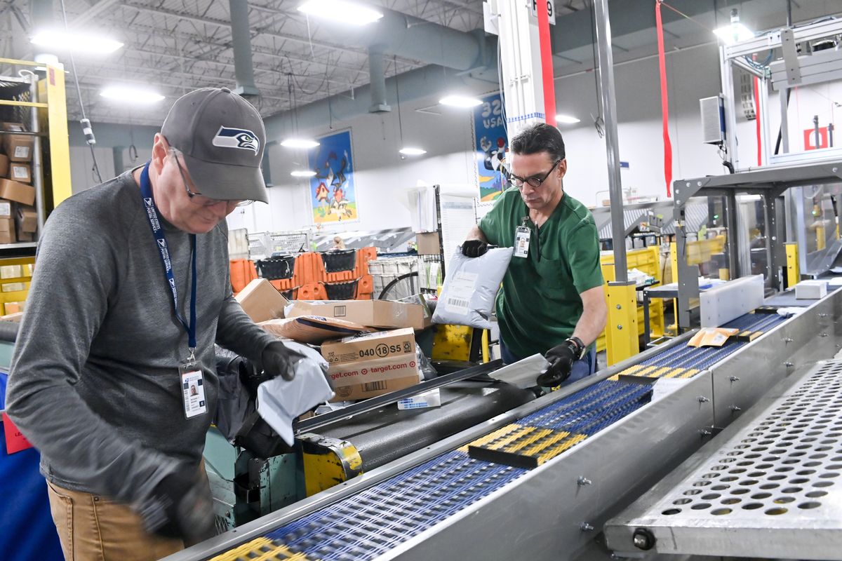 Postal workers Rich Brown and Stu McKenzie place packages on the Automated Delivery Unit Sorter, or ADUS, during a media tour Tuesday at the U.S. Postal Service’s Spokane Processing & Distribution Center near Spokane International Airport.  (Tyler Tjomsland/The Spokesman-Review)