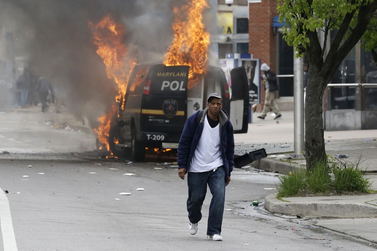 A man walks past a burning police vehicle, Monday, April 27, 2015, during unrest following the funeral of Freddie Gray in Baltimore. Gray died from spinal injuries about a week after he was arrested and transported in a Baltimore Police Department van. (Patrick Semansky / Associated Press)