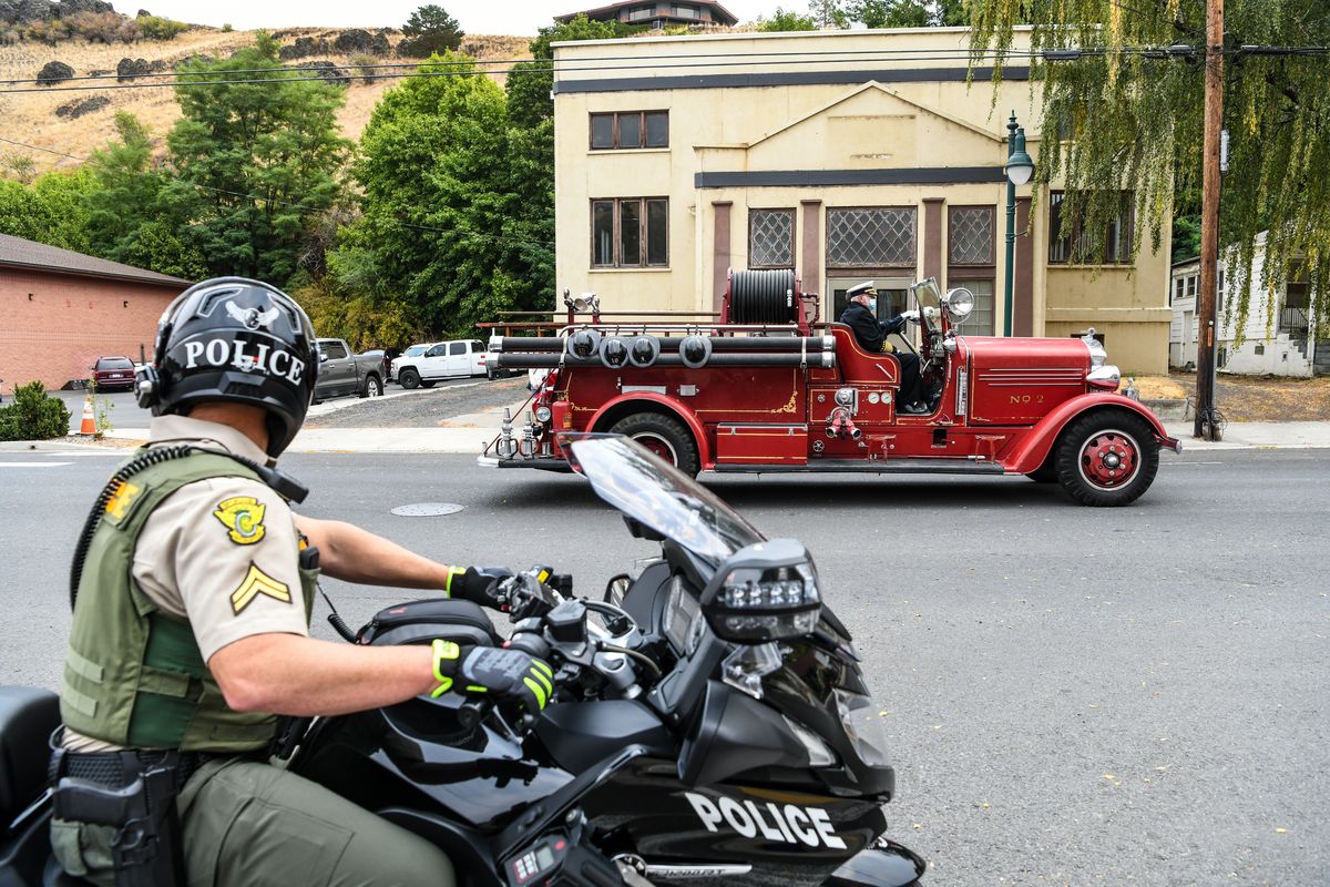 Spokane Valley Police officer Jeff Weiton controls traffic as an American LaFrance fire engine carries the body of longtime Colfax Firefighter Jim Krouse in the lead position of a 46 unit procession along Mill Street in Colfax, Friday, Sept. 10. 2021. Krouse died after experiencing a heart attack while on the scene of a fire.  (DAN PELLE/THE SPOKESMAN-REVIEW)