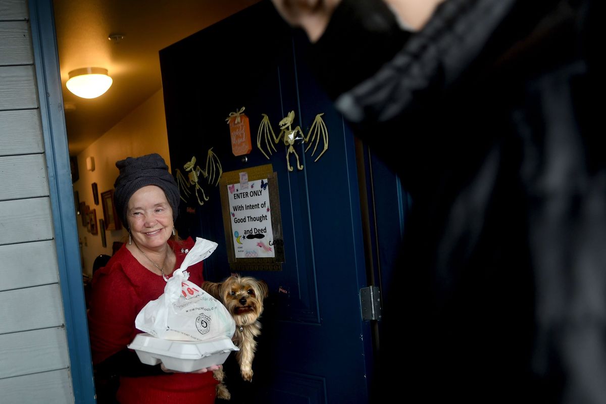 Dew Warnock holds her dog, Tank, as she receives a Thanksgiving meal from Austin Pugh, 19, as part of Feed Thy Neighbor and Meals on Wheels meal delivery on Thursday.  (Kathy Plonka/The Spokesman-Review)