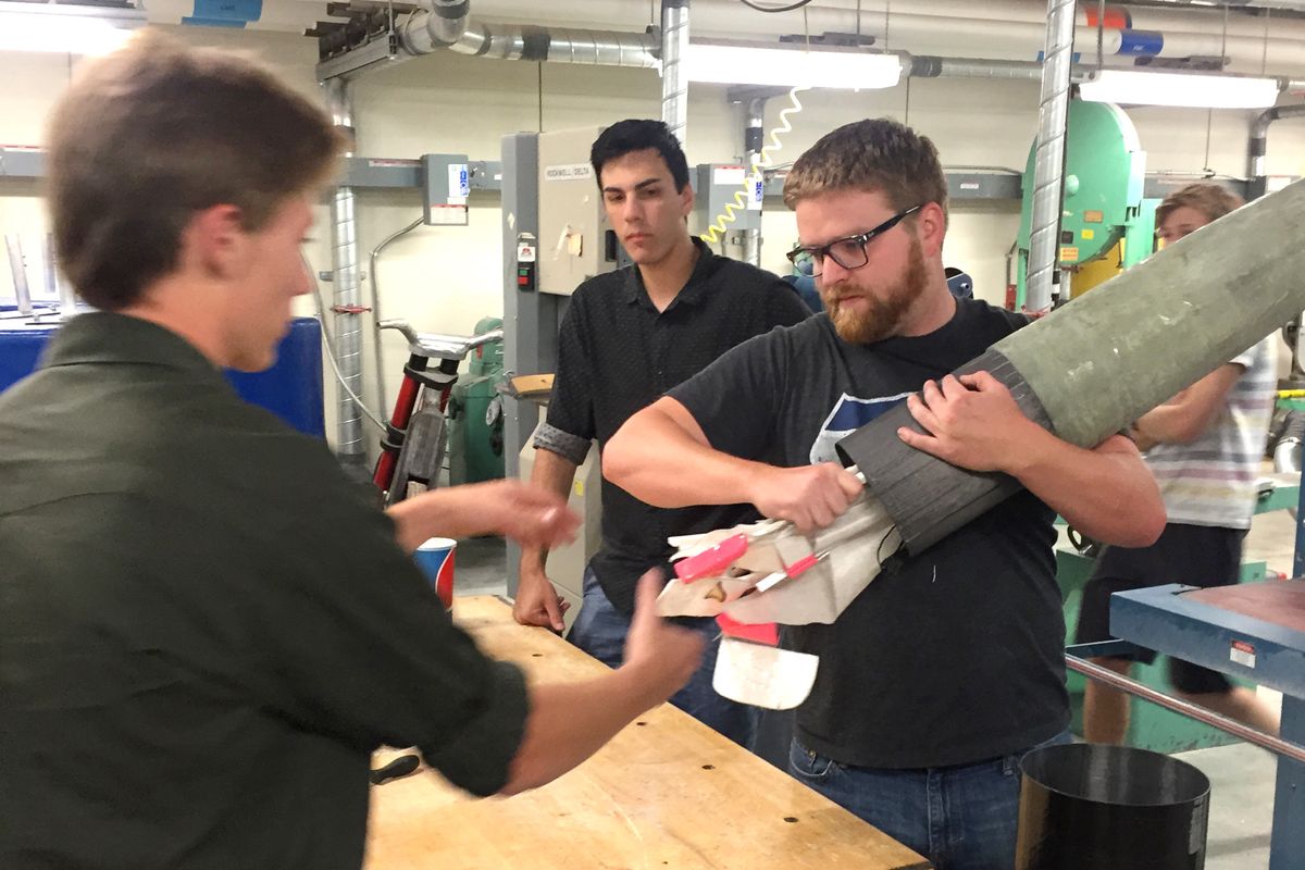 Eastern Washington University student Spencer Scott, right, practices tucking the collapsible airplane built by Riverpoint Academy students into the nose cone of the large rocket built recently at EWU.