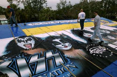 
Workers Charles Downing, left, and David Hooks, center, join homeowner Dana Morris on the roof of his house Saturday in Gulf Breeze, Fla., while installing an old billboard advertising a Kiss concert. 
 (Associated Press / The Spokesman-Review)