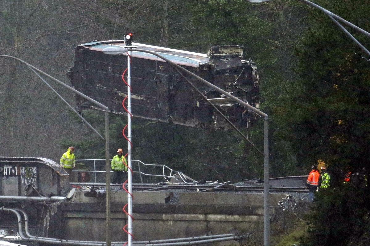 A damaged Amtrak train car is lowered from an overpass at the scene of a train crash onto Interstate 5 a day earlier, Tuesday, Dec. 19, 2017, in DuPont, Wash. Federal investigators say they don't yet know why the Amtrak train was traveling 50 mph over the speed limit when it derailed Monday south of Seattle. (Elaine Thompson / Associated Press)