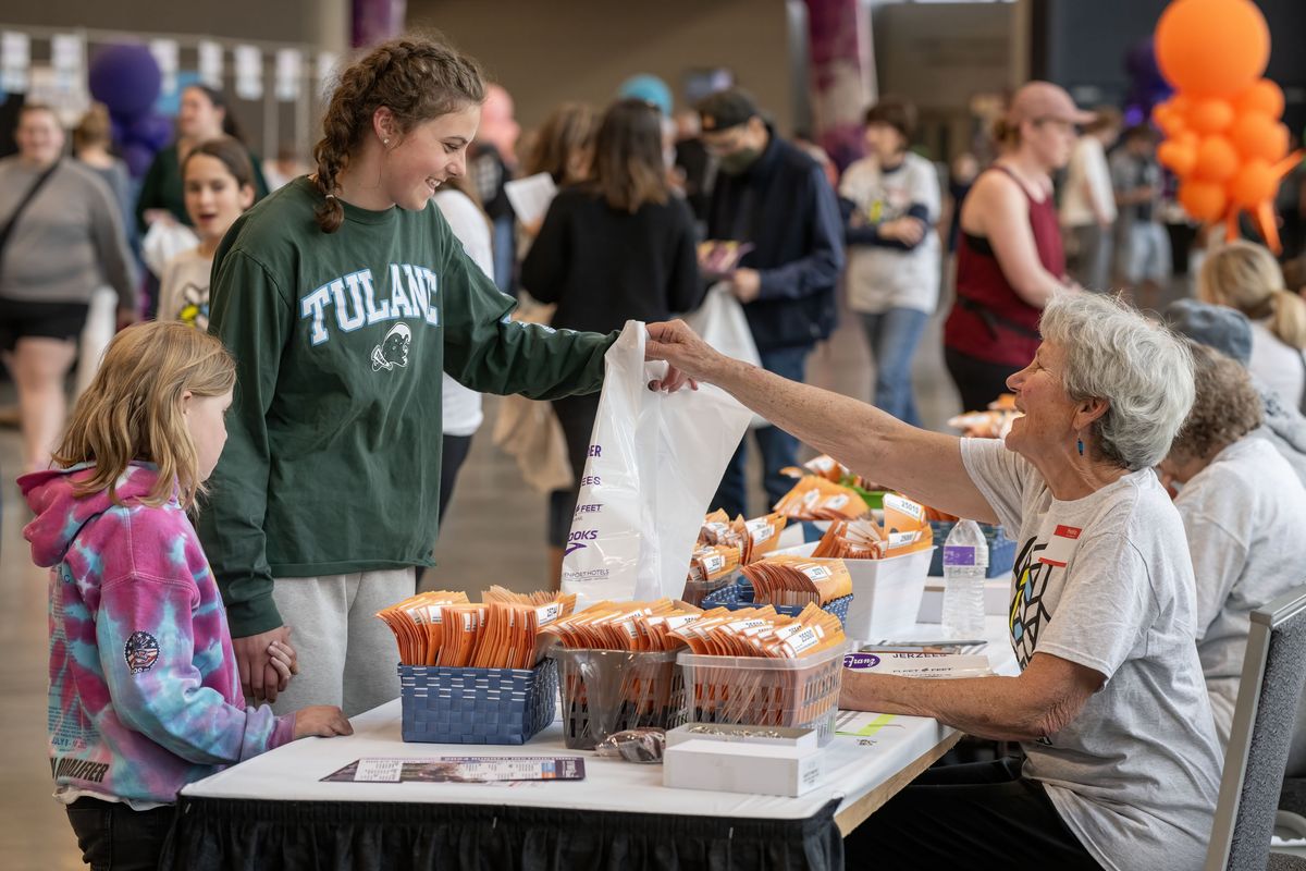 Keke Cleveland, 15, and her sister Quinn, 8, pick up their Bloomsday race packets from volunteer Robin Redman at the Spokane Convention Center Friday, May 3, 2024. After packet pickup, Bloomsday participants meandered through the annual trade show featuring running clothing, shoes and services for sale.  (COLIN MULVANY/THE SPOKESMAN-REVIEW)
