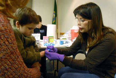 
Lucas Cusano, 4, watches as Hope Thommes, right, uses an auto lancing device to make a tiny hole in his finger tip to draw a drop of blood for blood lead testing  March 12  at East Central Community Center. The Lands Council, a regional environmental group, were offering free blood lead screenings for children, so parents, like Sherol Cusano, left, brought their children. 
 (Jesse Tinsley / The Spokesman-Review)