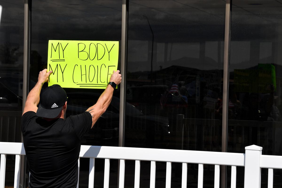 A man waves a sign outside the Central Valley School District’s office during a protest of COVID-19 masking regulations on Wednesday in Spokane Valley.  (Tyler Tjomsland/The Spokesman-Review)