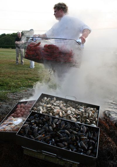 Shaughn Coyne, of McGrath Clambakes Inc., carries a crate containing 60 lobsters away from a pit of hot rocks, where the shellfish had steamed for two hours atop a mound of seaweed. (The Spokesman-Review)
