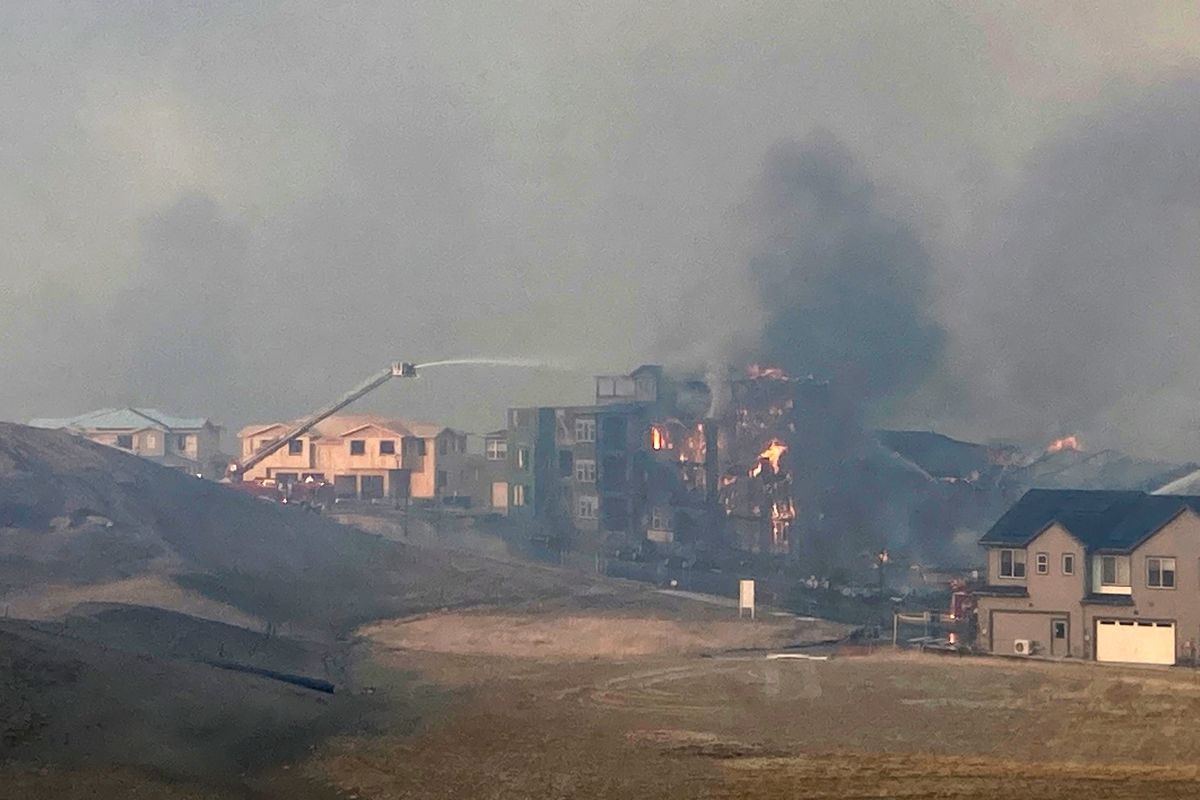 Firefighters spray water on a structure fire as a wildfire burns, Thursday, Dec. 30, 2021, in Superior, Colo. Thousands of residents in Superior and Louisville, two communities near Denver, were ordered to evacuate Thursday because of a wind-fueled wildfire that engulfed parts of the area in smoky, orangish skies.  (David Zelio)