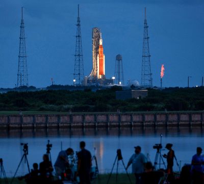 Photographers gather at dawn on launch day for Artemis I at Kennedy Space Center, Florida, on Saturday, Sept. 3, 2022. The flame, at far right, indicates fueling had begun on the heavy-lift rocket before the launch was scrubbed.  (TRIBUNE NEWS SERVICE)