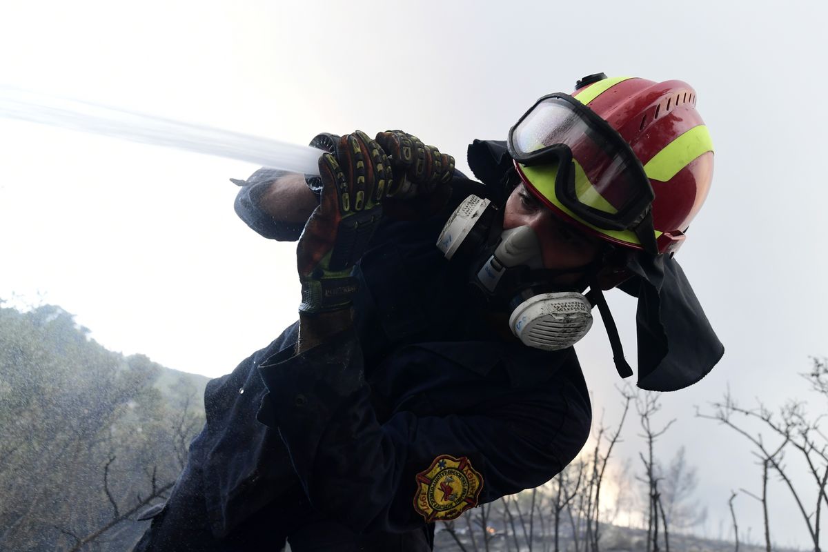 A firefighter tries to extinguish fire in Agios Stefanos, in northern Athens, Greece, Friday, Aug. 6, 2021. Thousands of people have fled wildfires burning out of control in Greece and Turkey, including a major blaze just north of the Greek capital of Athens that left one person dead.  (Michael Varaklas)