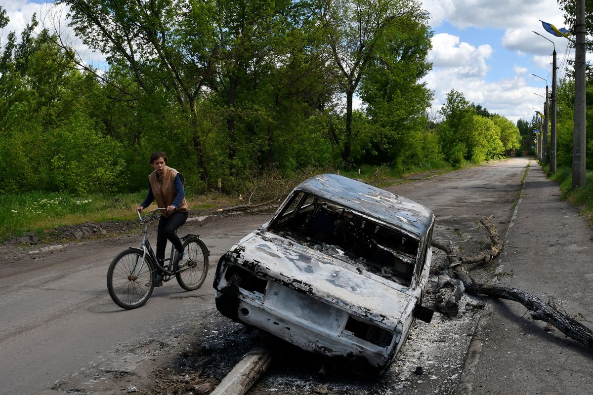 A man rides a bicycle past a car destroyed by shelling in a street in the village of Niu-York, Donetsk region, Ukraine, on May 16.  (Andriy Andriyenko)
