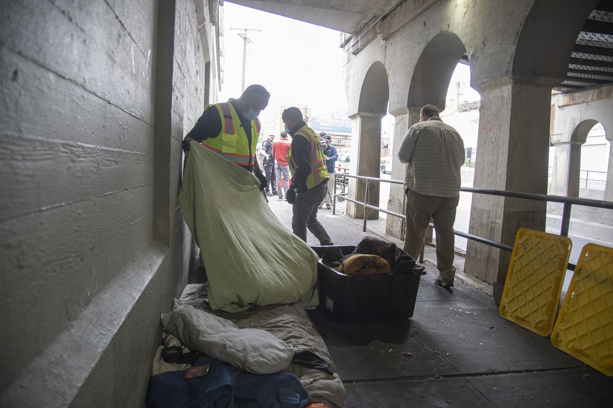 Members of the Spokane litter crew clean the Browne Street underpass, which is often a camping spot for homeless people, Wednesday, June 9, 2021 in downtown Spokane. The crew placed a pile of bedding into plastic totes as a courtesy to the owner of the belongings who was not present when the cleanup began. The city used police officers, a litter crew and employees of the Downtown Spokane Partnership to complete the cleanup.  (JESSE TINSLEY/THE SPOKESMAN-REVIEW)