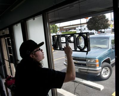 Daniel Wendling, of Satori, hangs an “Open” sign in the store’s window moments before opening its door for the first time Friday. Satori, on North Division Street, is the second state-licensed marijuana retailer to open for business in Spokane. (Dan Pelle)