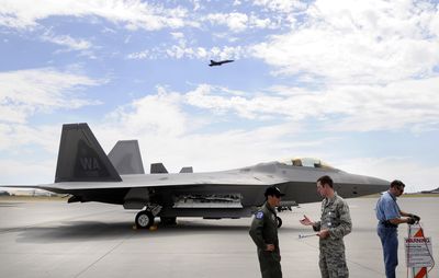 Maj. Paul Moga, left, talks with Lt. Tristan Hinderliter of Fairchild Air Force Base’s public affairs office in front of an Air Force F-22 Raptor on the base Thursday,  as a Blue Angels F/A-18  aircraft roars overhead.  Below, the Blue Angels fly in formation over the West Plains.  (Photos by Jesse Tinsley / The Spokesman-Review)