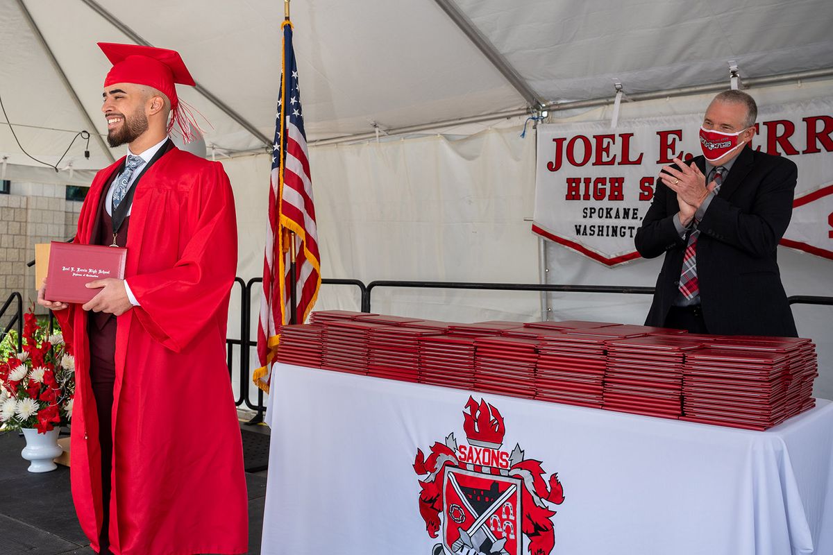 In this June 6, 2020 photo, Ferris High School senior Mustafa Amer Al Sabahi pauses to let his family take his photo from their car after receiving his diploma from principal Ken Schutz during the school’s drive-thru graduation ceremony.  (COLIN MULVANY/THE SPOKESMAN-REVIEW)