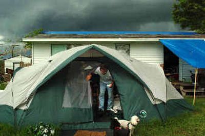 
Phillip Deaton emerges from a tent that is his temporary home, as thick rainclouds gather Wednesday over his Punta Gorda, Fla., house, which was damaged during Hurricane Charley.
 (Associated Press / The Spokesman-Review)