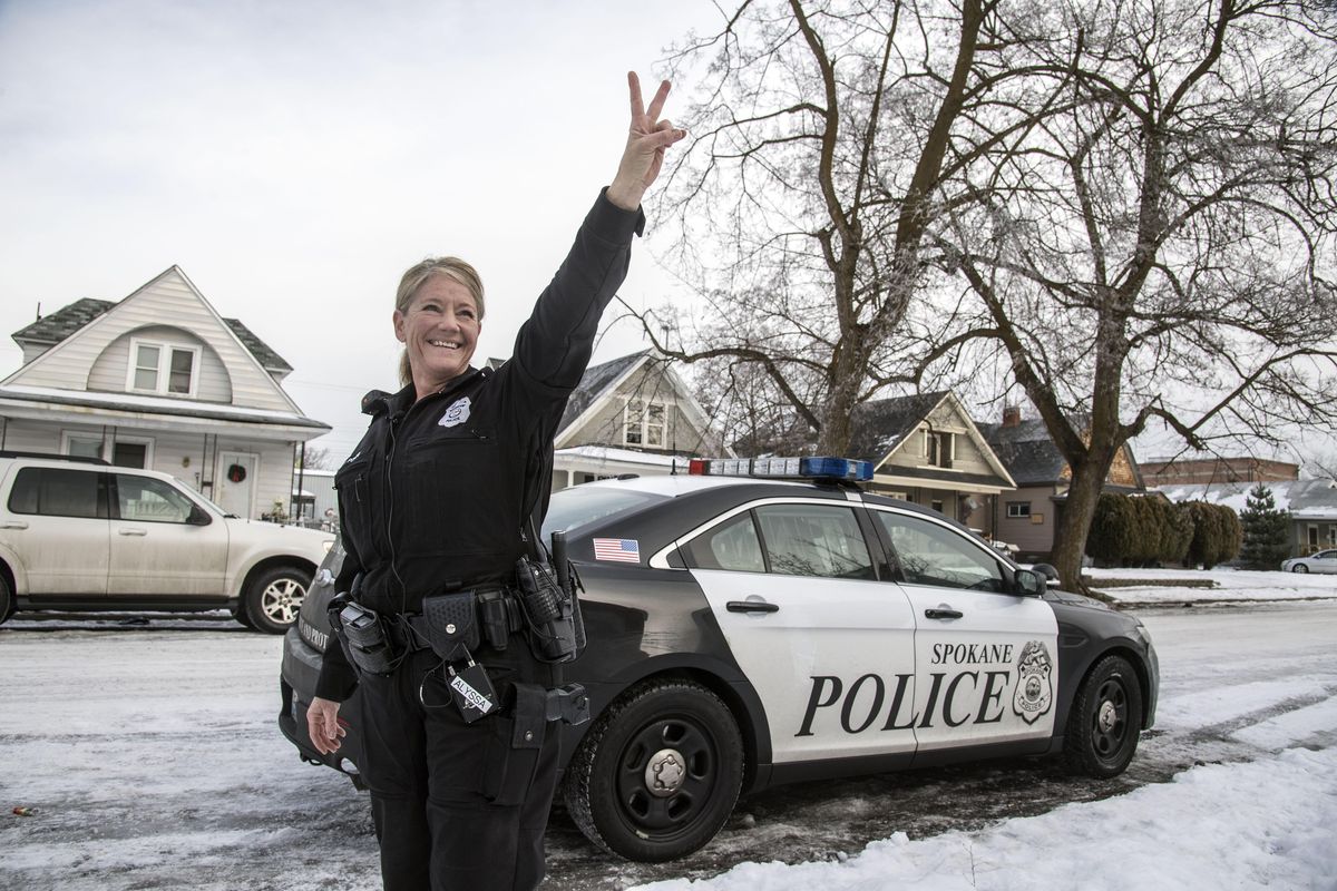 Spokane Police resource officer Traci Ponto flashes her signature peace sign to children in a second-floor window in the West Central neighborhood after delivering a Christmas gift to a  family, Dec. 22, 2016. (Dan Pelle / The Spokesman-Review)
