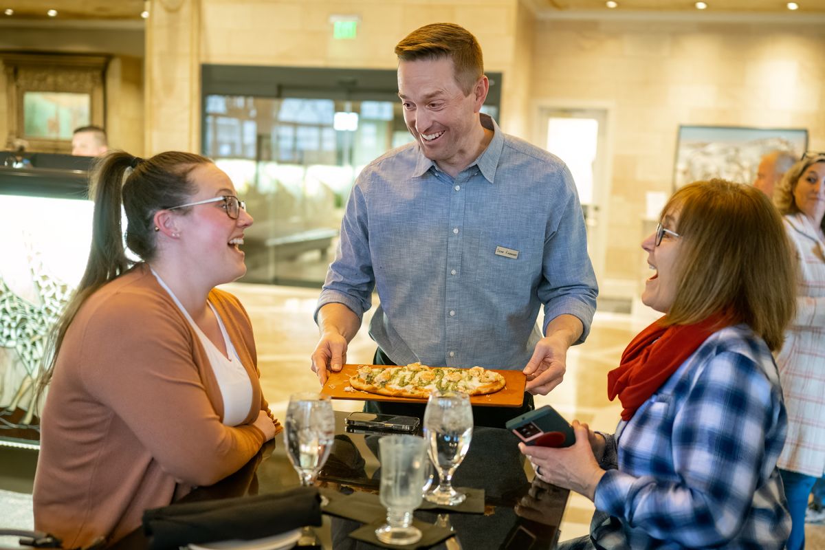 ESPN Basketball Analyst Sean Farnham – who has been calling nearby Gonzaga basketball games since 2010 – serves up a Farnham Flatbread to Kendra Gardner, on left and her mother Teri Gardner at the Davenport Tower’s Safari Room, Friday, Feb. 10, 2023. A portion of all ‘Farnham Flatbread’ proceeds from the event (and throughout March Madness) will benefit Coaches vs. Cancer – with the goal of raising $20K.  (COLIN MULVANY)