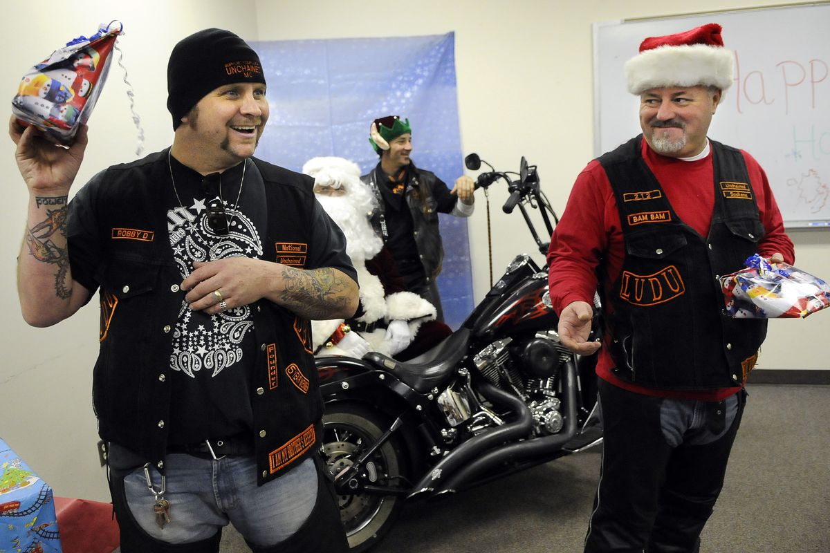 Robert Deitrick, 42, of the Unchained Brotherhood, hands out a Christmas present during a holiday party Friday at the Institute for Extended Learning in Hillyard. Deitrick, along with members Robert Edens, 42, center, and Beau Grillo, 46, welcomed children and families of IEL students.  (Dan Pelle)