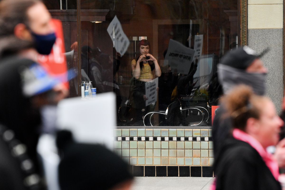 A woman inside Bliss Hair Studio gestures to marchers as they pass on Saturday during a Humans for Housing march held by Humanizing Spokane.  (Tyler Tjomsland/The Spokesman-Re)