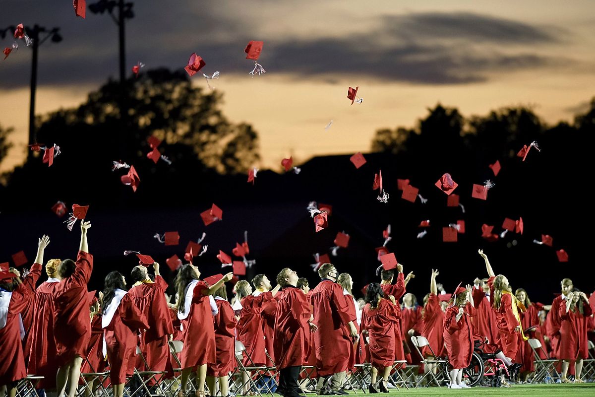 FILE - Red mortarboards fly into the evening sky at Heritage High School