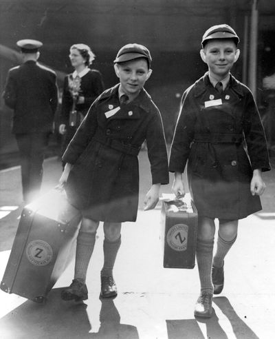 In this 1950 photo,  10-year-old twins Brian Thomas Sullivan  and Kevin James Sullivan from Islington, London,  carry their luggage to the boat train  as they leave  London bound for Auckland, New Zealand.  (File Associated Press)