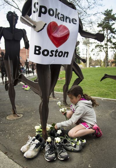 During a memorial to the victims of the Boston Marathon bombing, Madison Sandifur, 7, places white roses into donated running shoes at the base of the running sculptures in Riverfront Park in Spokane on Tuesday. The shoes will be donated to Crosswalk Teen Shelter, Hope House and other organizations. (Colin Mulvany)