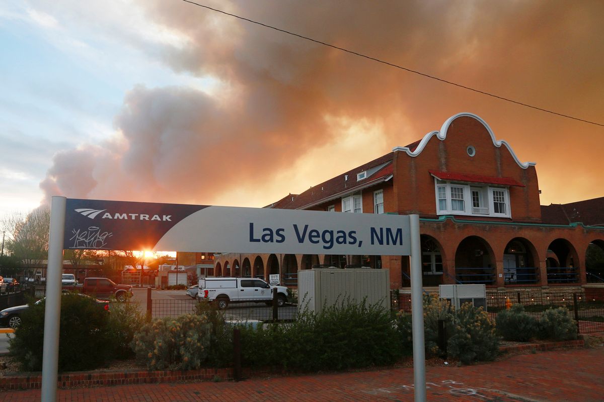 A sunset seen through a wall of wildfire smoke from the Amtrak train station in Las Vegas, N.M., on Saturday. The Castañeda Hotel, right, hosted meals for residents and firefighters this week with sponsorships from restaurants and other businesses.  (Cedar Attanasio)