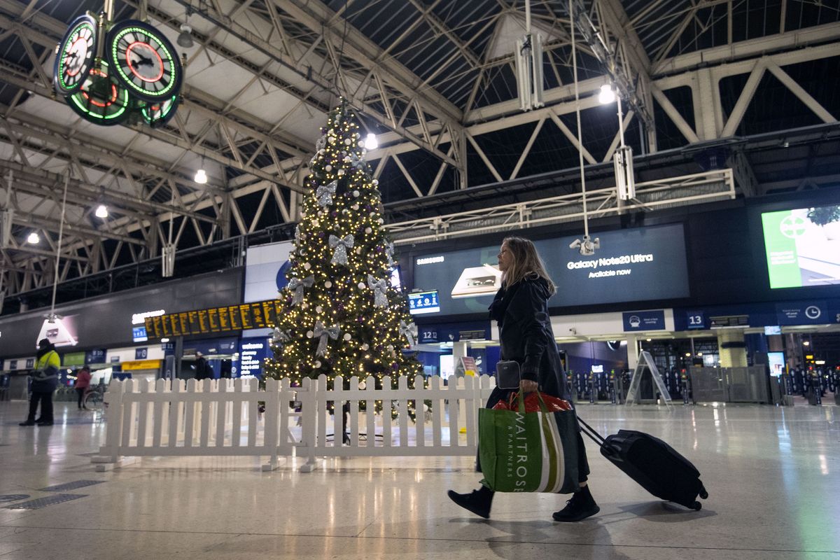 A woman pulls a suitcase past the Christmas tree on the concourse of Waterloo Station in central London, Sunday, Dec. 20, 2020. Millions of people in England have learned they must cancel their Christmas get-togethers and holiday shopping trips. British Prime Minister Boris Johnson said Saturday that holiday gatherings can’t go ahead and non-essential shops must close in London and much of southern England.  (Victoria Jones)