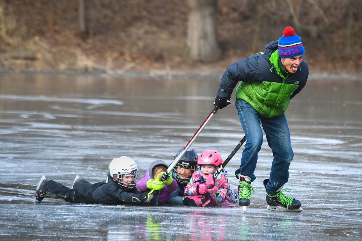 Aaron Scott puts his hockey skills to the test as he uses a pair of sticks to slide, from left, Colton Fisch, 5, Winnie Scott, 4, Graeme Scott, 6, and Darby Quinn, 4, across the frozen Cannon Hill Park pond during the freezing temperatures of Thursday afternoon, Feb. 11, 2021, in Spokane.  (Dan Pelle/THESPOKESMAN-REVIEW)
